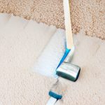 A looking-down view of a rug that has been partially painted white by a paint roller, with a portion of the unpainted rug visible in the top right corner.